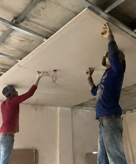Two technicians fixing gypsum board to a ceiling frame